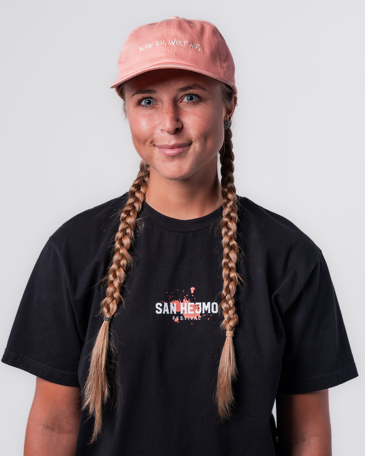 Eine Frau trägt das schwarze Line-up T-Shirt und die Apricot farbige Dad Cap. Sie steht gerade zur Kamera. Vorne mittig auf der Cap sind die Worte "Musik an, Welt aus" in weiß in Großbuchstaben gestickt.