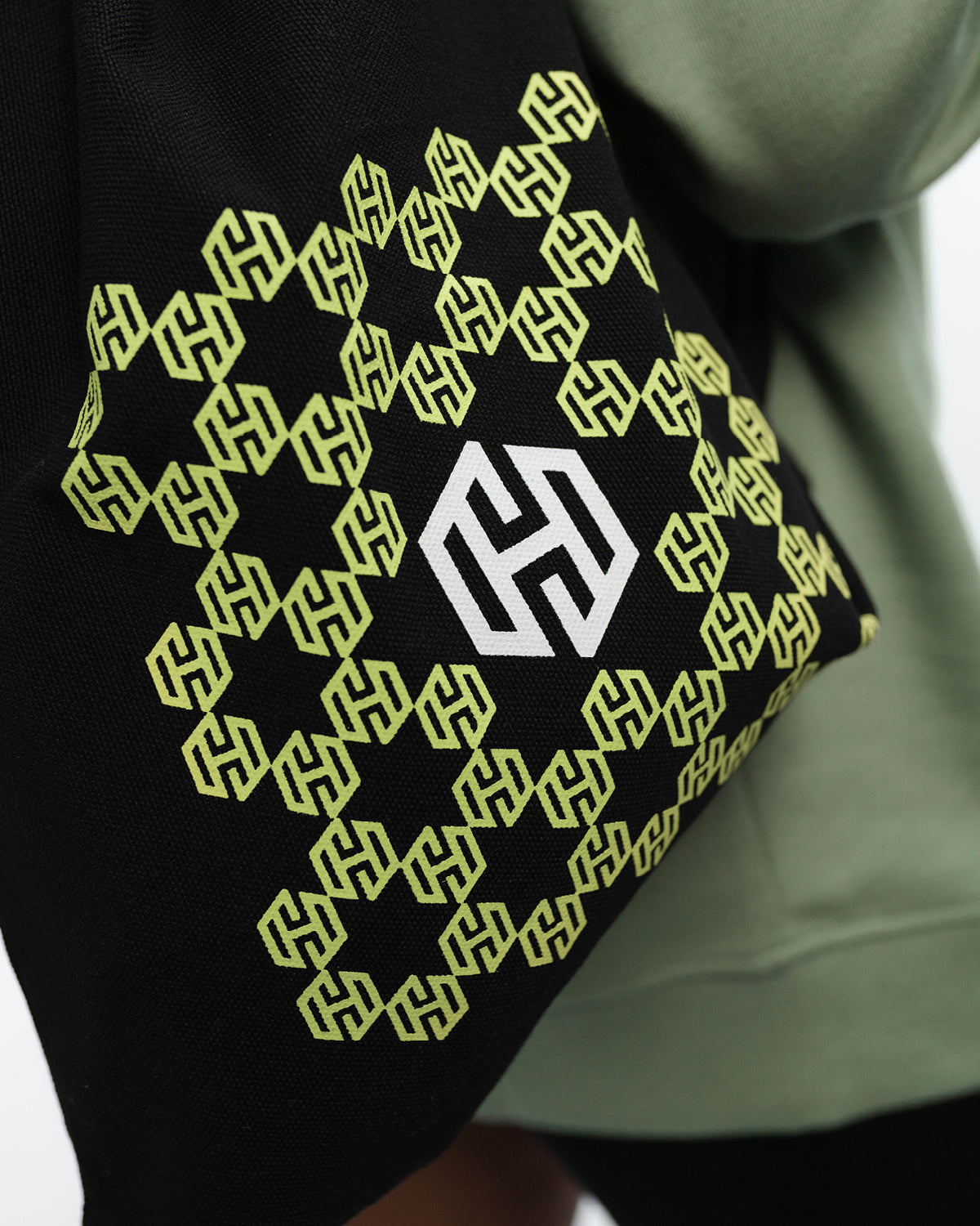 Eine Nahaufnahme des schwarzen sportlichen Beutel mit dem in Bienenwaben angeordneten San Hejmo Logo in Mint. Mittig ist das San Hejmo in Weiß abgebildet.