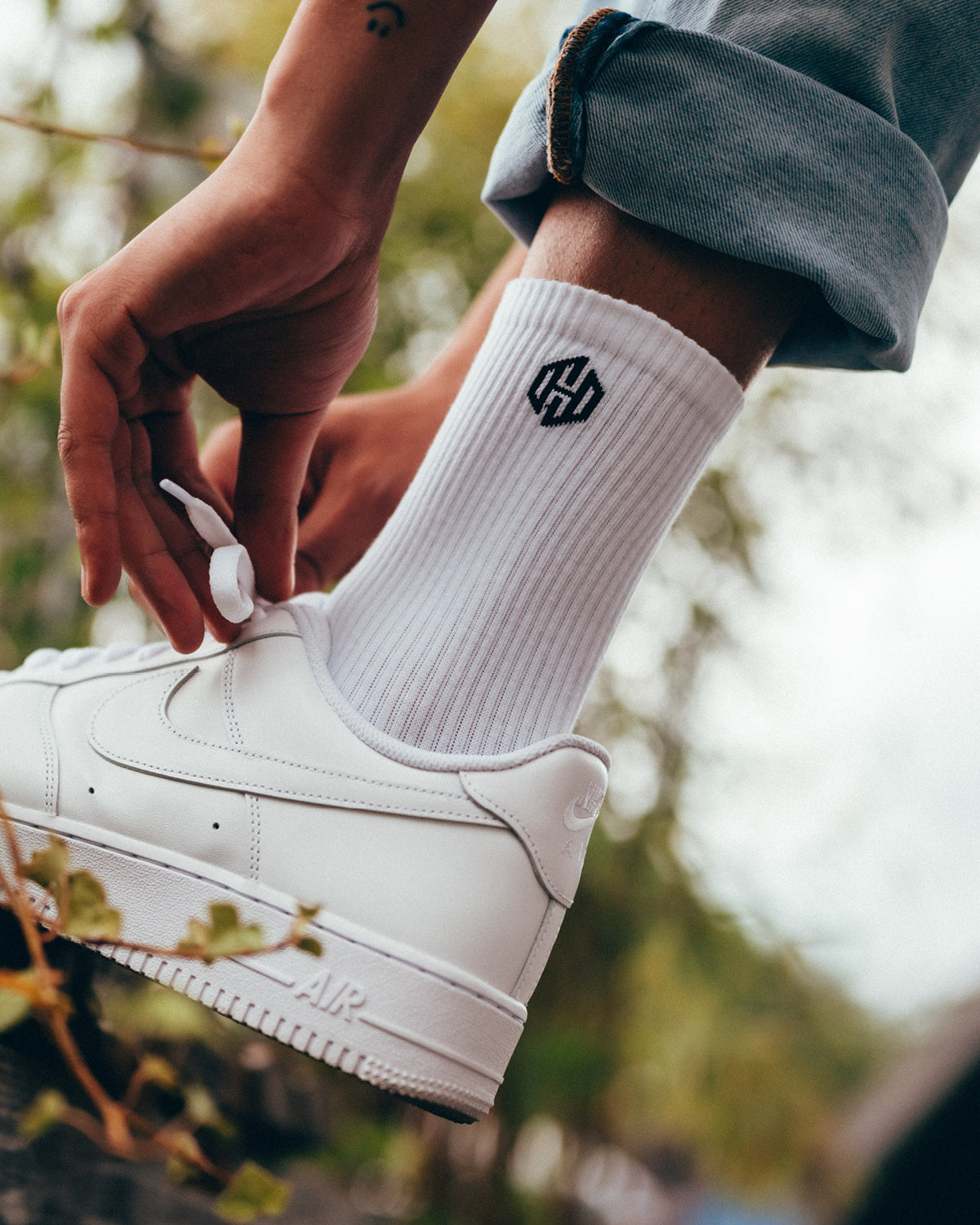 Ein Model trägt weiße Tennissocken mit dem San Hejmo Signet Logo an der Seite auf Knöchelhöhe.