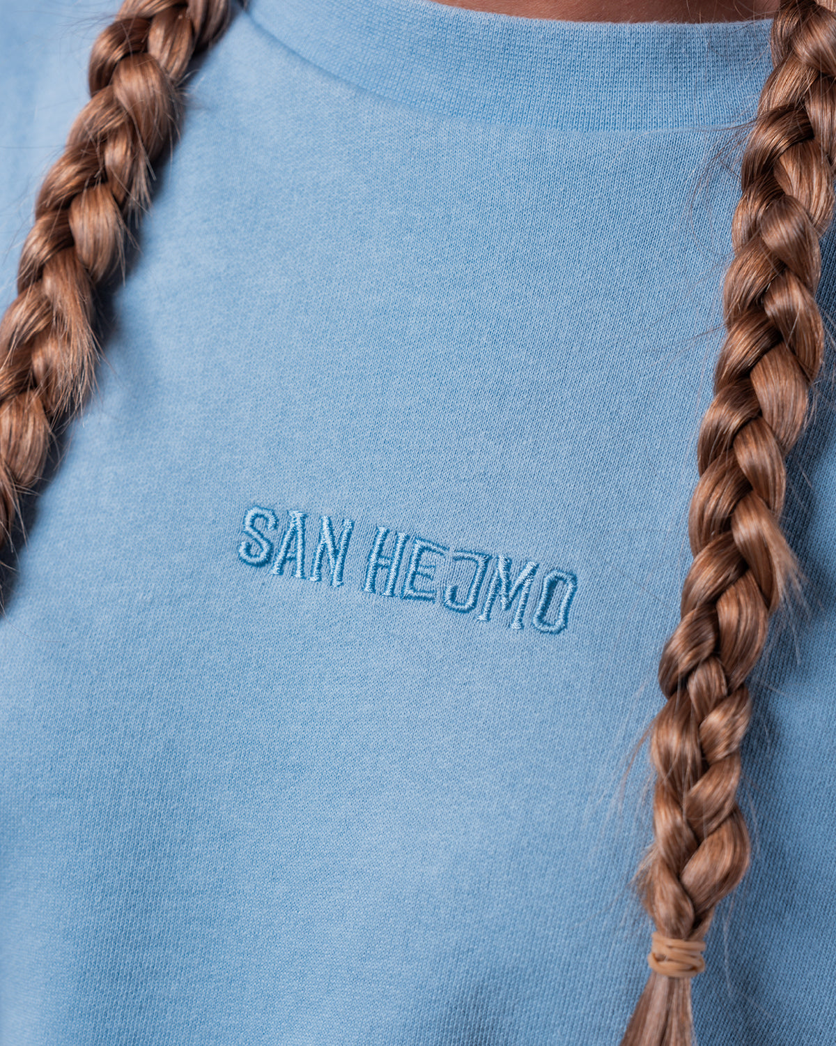 Der Cut Out Sweater in Nahaufnahme mit Fokus auf den Stick in der Mitte des Sweaters. Dieser zeigt den Schriftzug "San Hejmo" ebenfalls in hellblauer Farbe.