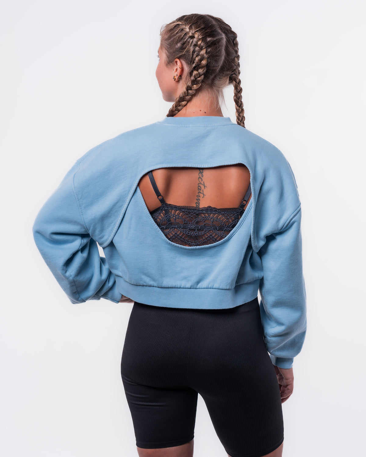 Zu sehen ist eine junge Frau. Sie trägt den neuen "Cut Out" Sweater in hellblau und eine schwarze Radler Hose und steht vor einer weißen Wand. Der Sweater hat am Rücken eine Öffnung die sich über die untere Hälfte der Schulterblätter hin zum Mittleren Rücken erstreckt.