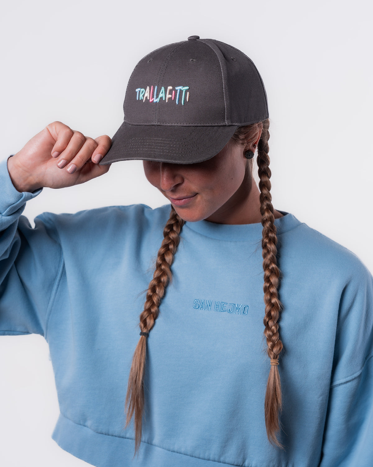 Eine Frau trägt den Cut-Out Sweater und die Anthrazitfarbige Trallafitti Cap. Vorne Mittig auf der Cap sind die Worte "Trallafitti" in bunt und in Großbuchstaben gestickt.