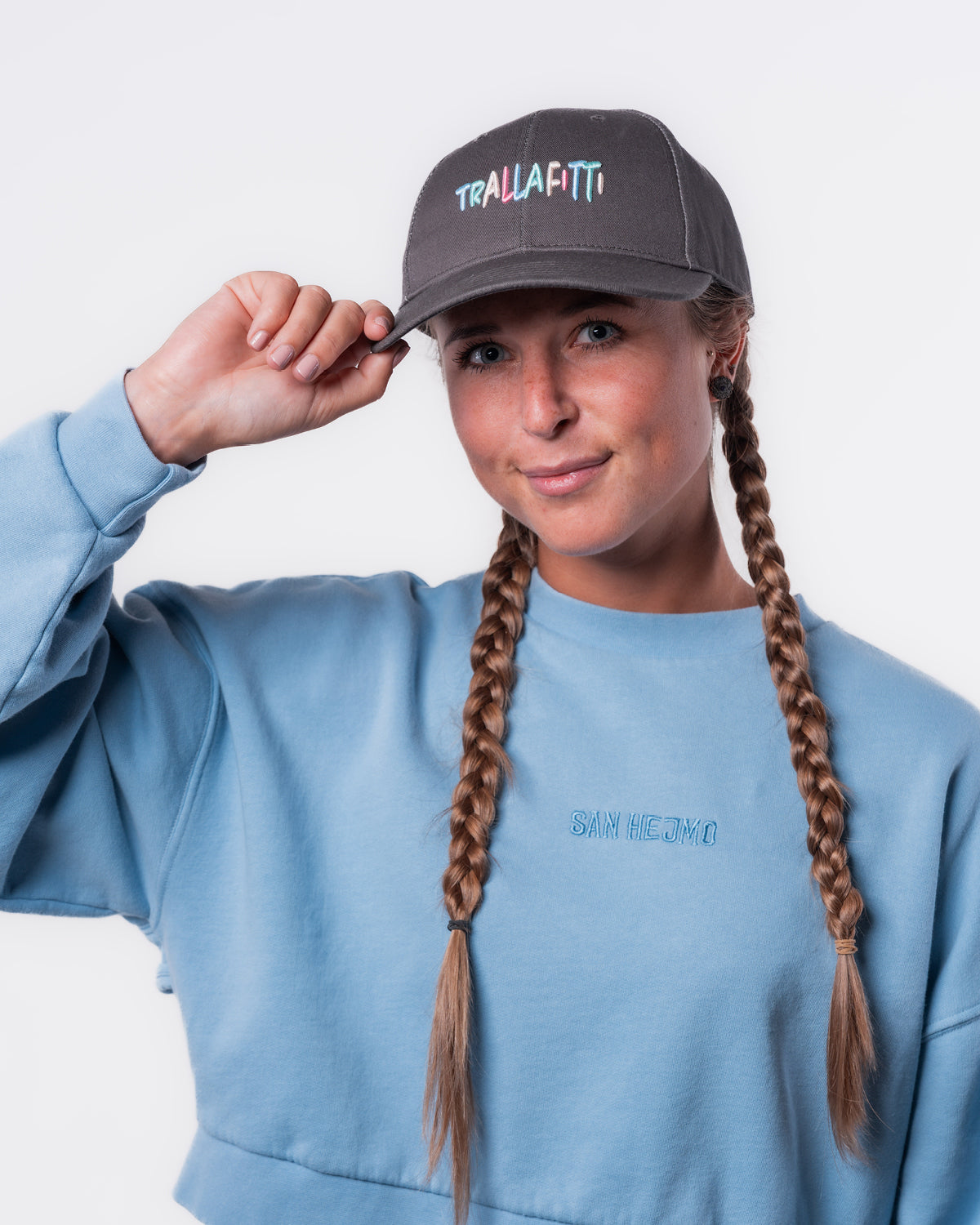 Eine Frau trägt den Cut-Out Sweater und die Anthrazitfarbige Trallafitti Cap. Vorne Mittig auf der Cap sind die Worte "Trallafitti" in bunt und in Großbuchstaben gestickt.