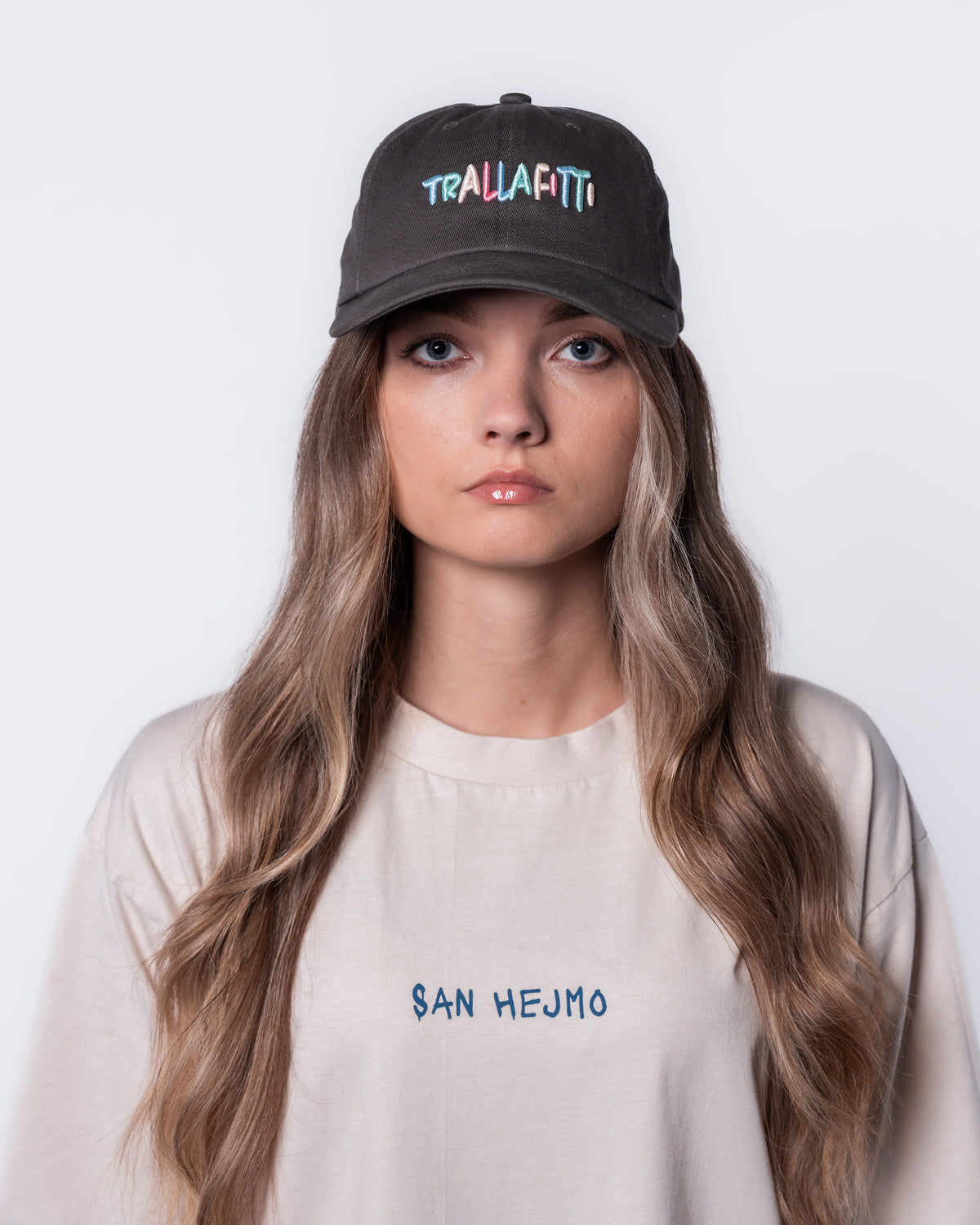 Eine Frau trägt den Cut-Out Sweater und die Anthrazitfarbige Trallafitti Cap. Vorne Mittig auf der Cap sind die Worte "Trallafitti" in bunt und in Großbuchstaben gestickt.