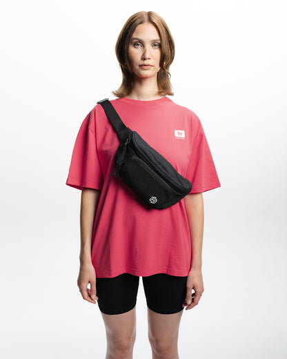 Eine Frau trägt ein pinkes Oberteil und schwarze Radlershorts und dazu die San Hejmo Bauchtasche quer über ihren Oberkörper. 