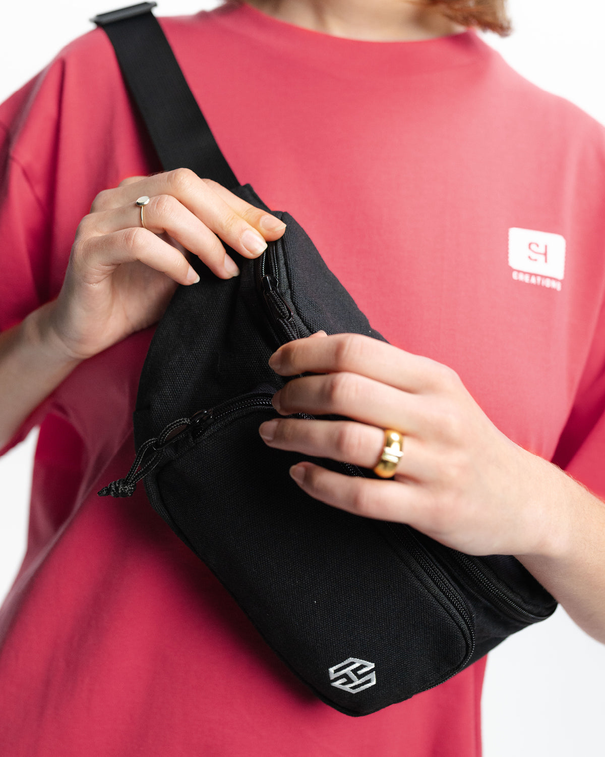 Einer Frau trägt die Bauchtasche von San Hejmo quer über ihren Oberkörper. Sie trägt ein pinkes Oberteil. Sie ist gerade dabei die Bauchtasche auf oder zuzumachen.