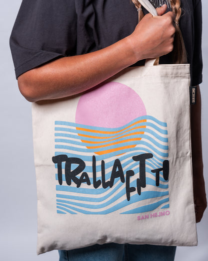 Ein naturbelassener beigefarbener Beutel mit der schwarzen Aufschrift „Trallafitti“. In einem künstlerischen Stil ist hinter diesen Worten ein Sonnenuntergang einer rosa Sonne am Meer zu erkennen. Die blauen Wellen sind als diverse Linien dargestellt.