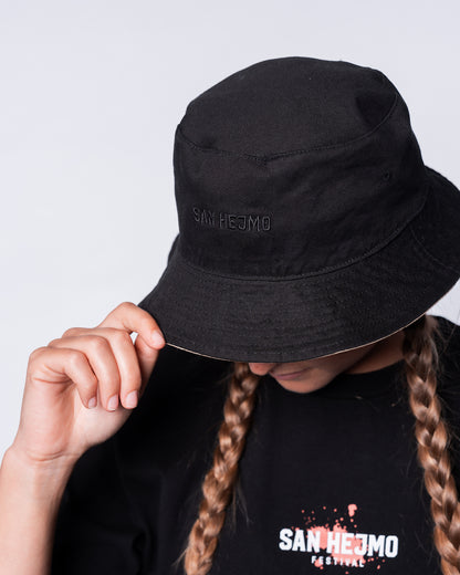 Die andere Seite des wendbaren Bucket Hats. Sie ist schwarz mit einem schwarzen Stick der Worte „San Hejmo“