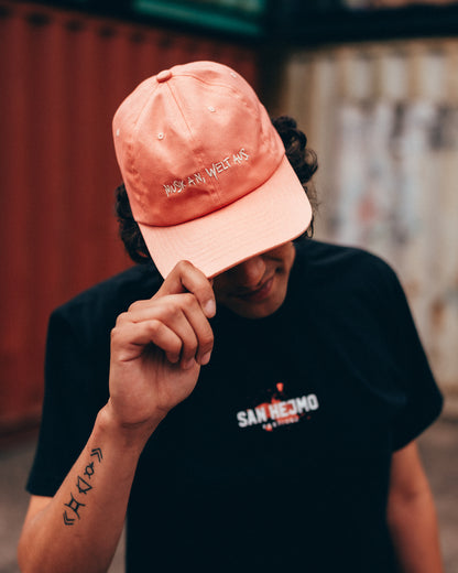Ein Mann vor einer Containerwand trägt das Line-up T-Shirt und die Apricot farbige Dad Cap. Er hält die Cap mit einer Hand tiefer in sein Gesicht. 