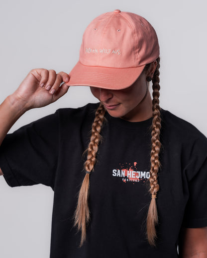Eine Frau trägt das schwarze Line-up T-Shirt und die Apricot farbige Dad Cap. Mittig vorne auf der Cap sind die Worte "Musik am, Welt aus" in Großbuchstaben gestickt. 