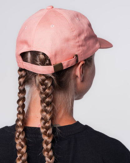 Eine Frau trägt das schwarze Line-up T-Shirt und die Apricot farbige Dad Cap. Sie steht mit dem Hinterkopf zur Kamera. Hinten links wird die Cap mit einem Strapback-Verschluss.