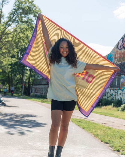 Eine Frau läuft über eine Straße und hat die San Hejmo Flagge in der Hand, diese hält sie ausgestreckt über sich. 