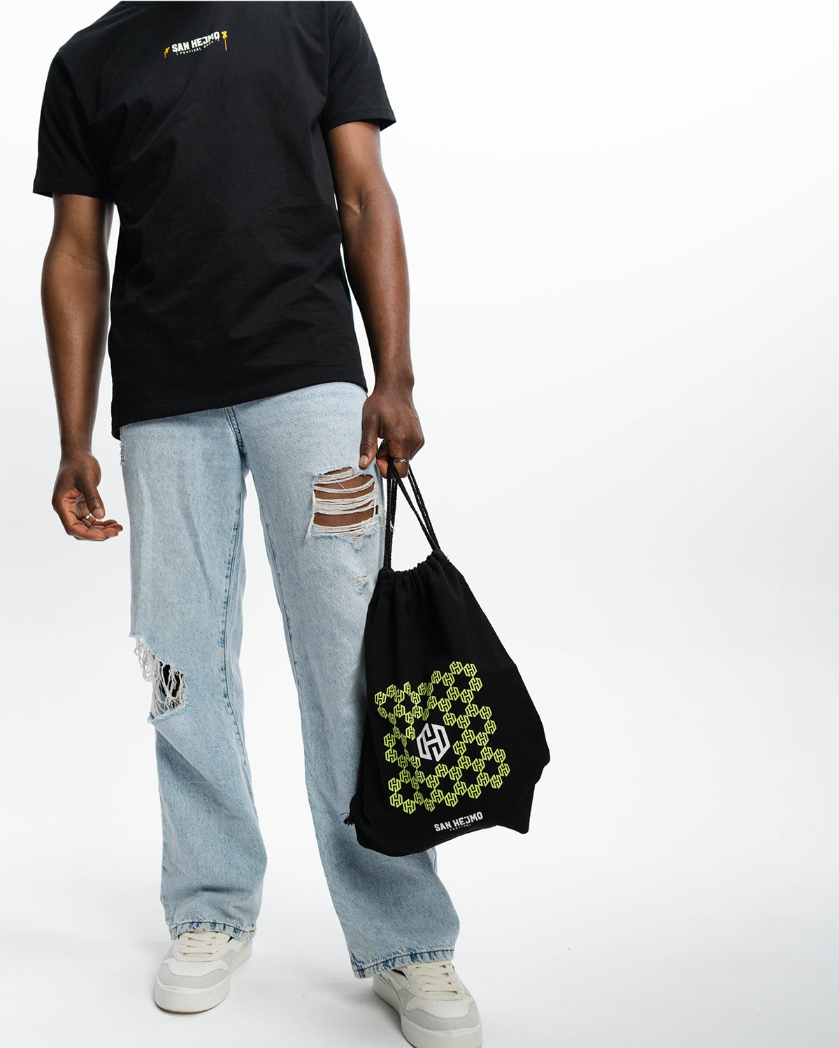 Ein schwarzer sportlicher Beutel mit dem in Bienenwaben angeordneten San Hejmo Logo in Mint. Mittig ist das San Hejmo in Weiß abgebildet. Ein Mann trägt ihn an beiden Bändern in der Hand.