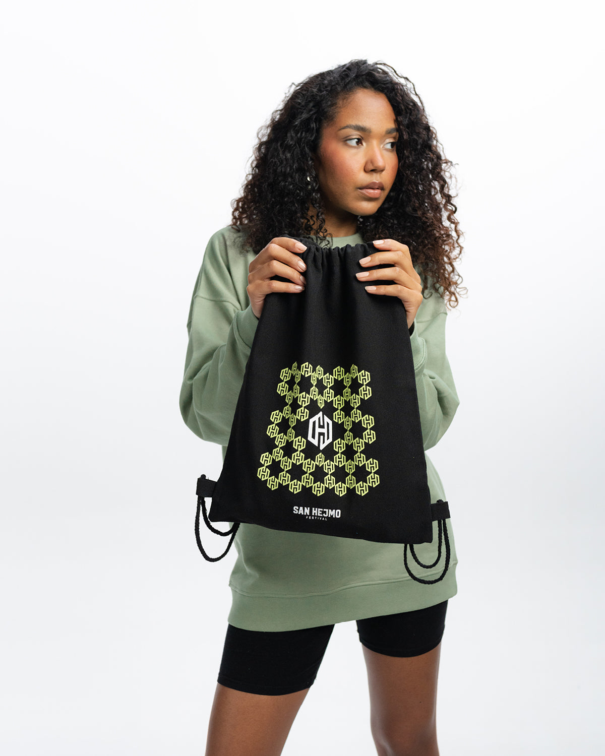Eine Frau hält den San Hejmo Sportbeutel in der Hand. Unter dem in Bienenwaben angeordneten Logo stehen die Worte "San Hejmo Festival" in weiß geschrieben.