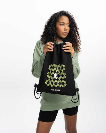 Eine Frau hält den San Hejmo Sportbeutel in der Hand. Unter dem in Bienenwaben angeordneten Logo stehen die Worte "San Hejmo Festival" in weiß geschrieben.