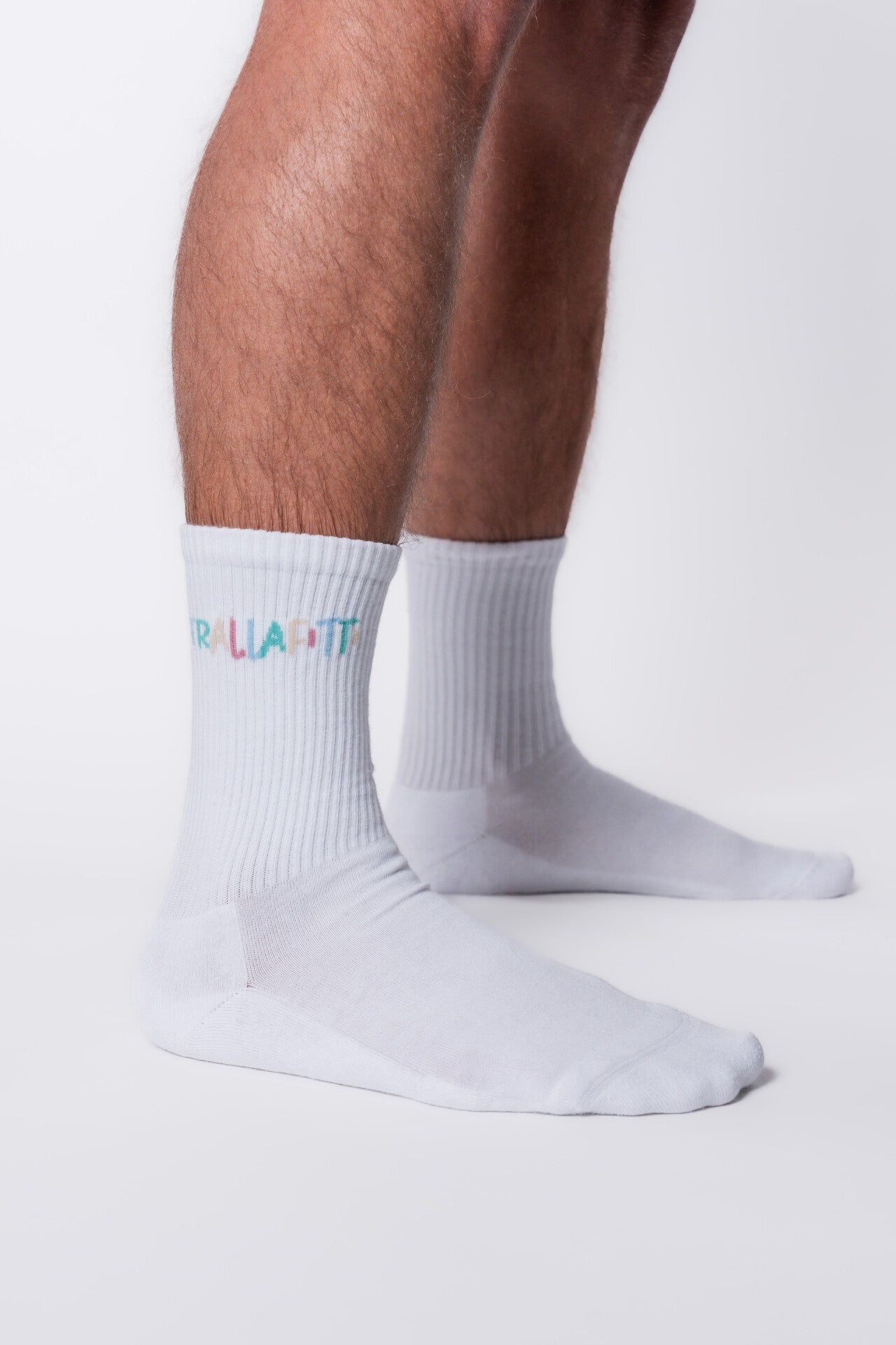  Zu sehen sind weiße hochgezogene Tennissocken die die seitliche Aufschrift „Trallafitti“ tragen. Die Buchstaben dieser Aufschrift haben jeweils verschiedene Pastellfarben.