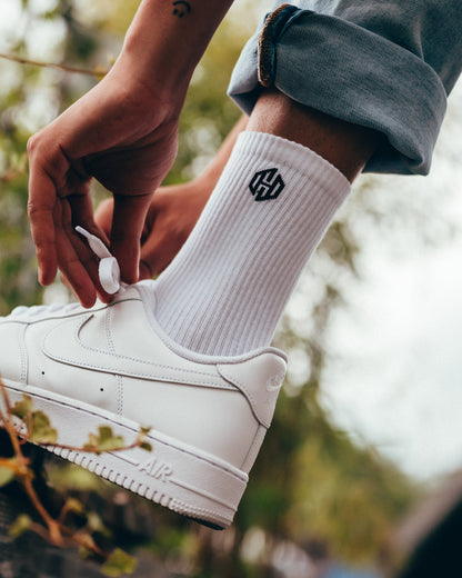 Ein Model trägt weiße Tennissocken mit dem San Hejmo Signet Logo an der Seite auf Knöchelhöhe. 
