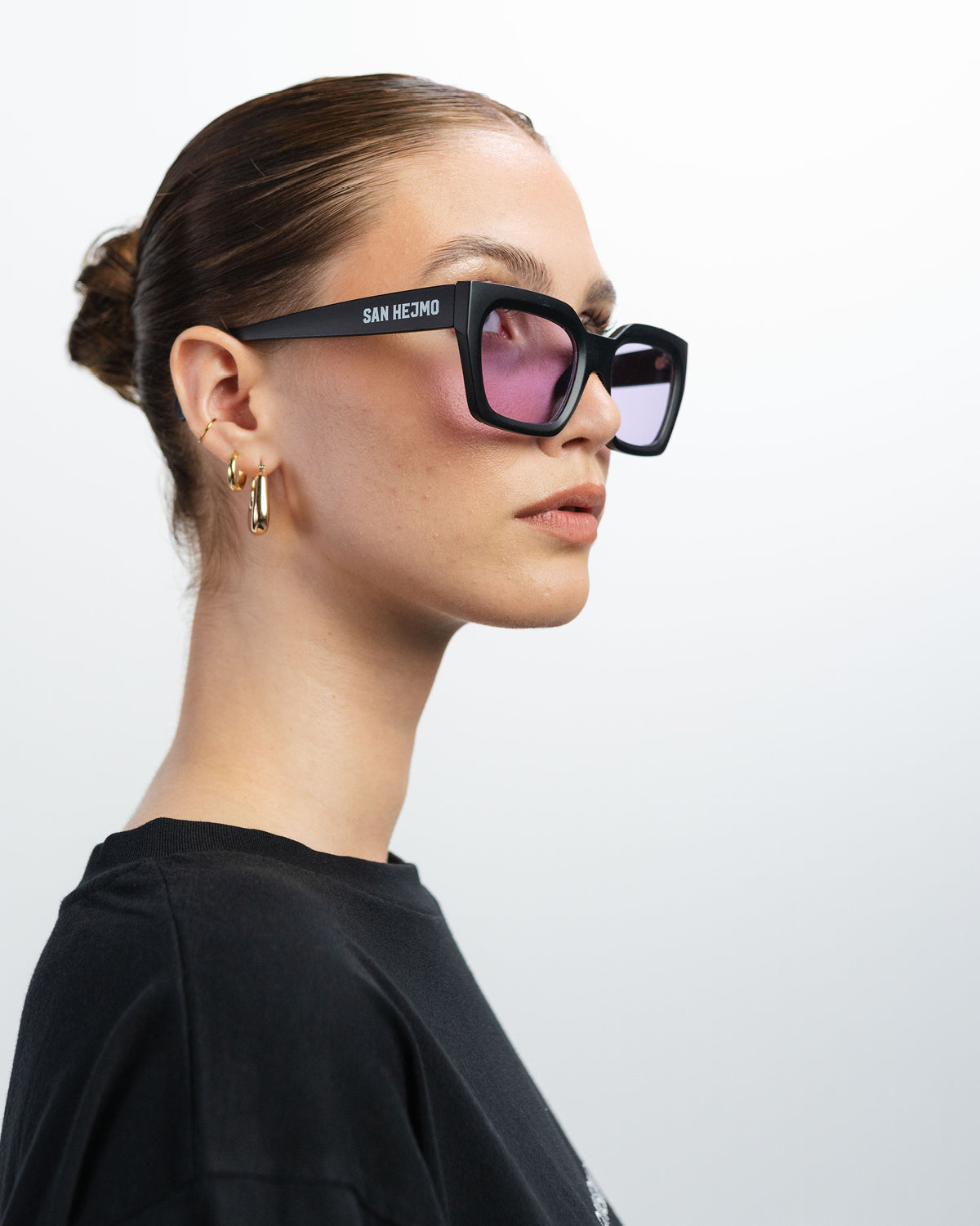 Eine Sonnenbrille mit einem eckig gehaltenen schwarzem Rahmen und rosa Gläsern. Sie wird von einer Frau getragen. Das Seitenprofil der Brille ist zu erkennen.