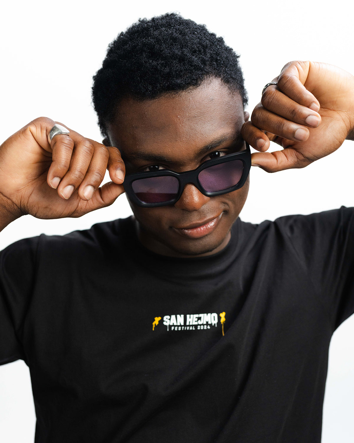 Eine Sonnenbrille mit einem eckig gehaltenen schwarzem Rahmen und rosa Gläsern. Sie wird von einer Mann getragen. 