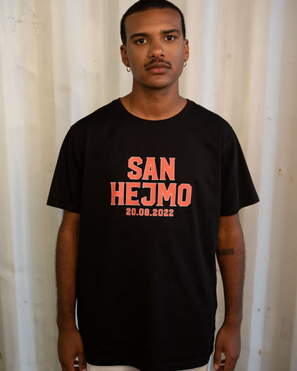 Das schwarze Line-up T-Shirt 2022, getragen von einem Mann. Es trägt die orangene Aufschrift "San Hejmo 20.08.2022". Die Schrift hat einen weißen Rahmen