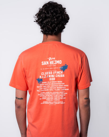 Auf dem T-Shirt ist das Line-up des Jahres 2025 zu sehen. Es ist in weißer Schrift gedruckt. Über dem Line-up ist das San Hejmo Logo gedruckt. Oben rechts und mittig links ist die Schrift mit jeweils einem blauen Farbklecks hinterlegt. 